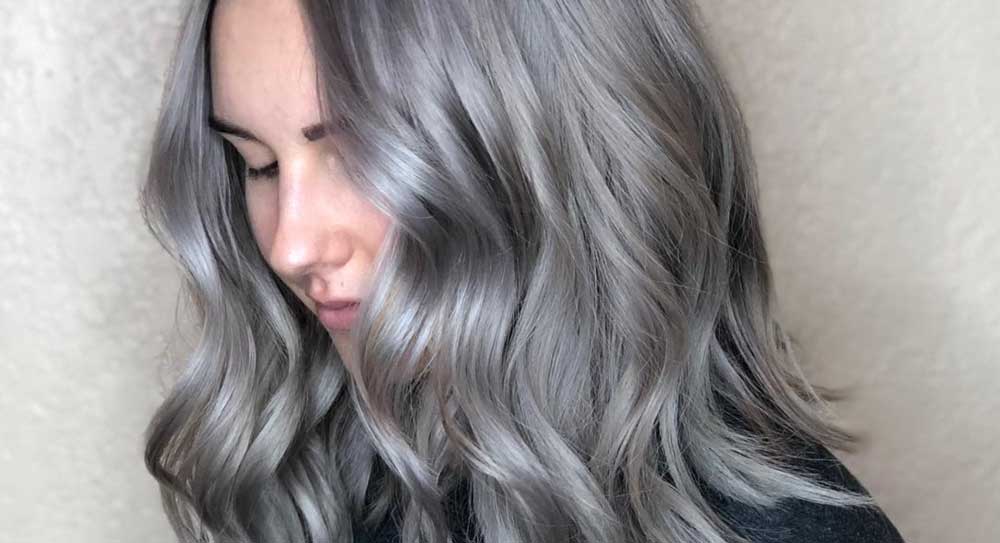 A woman with long, wavy silver hair styled at a salon looking downward. - K. Charles & Co. in San Antonio and Schertz, TX