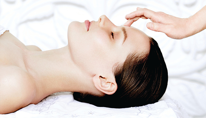 A woman receiving a facial treatment with a hand applying product to her forehead in a serene, spa-like setting, while her hairstyle is elegantly arranged to highlight the relaxation process. - K. Charles & Co. in San Antonio and Schertz, TX