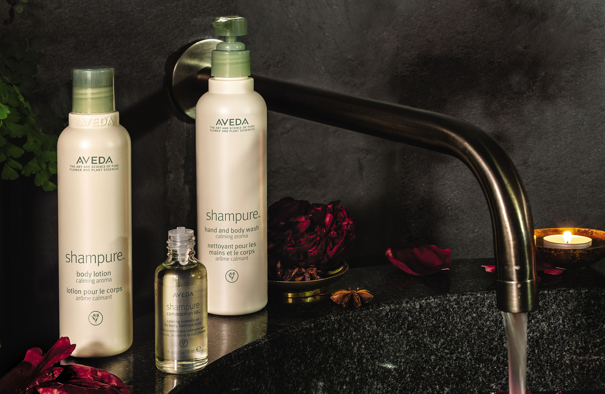 Two aveda shampure products on a dark bathroom counter with a faucet, rose petals, and a lit candle in the background. - K. Charles & Co. in San Antonio and Schertz, TX
