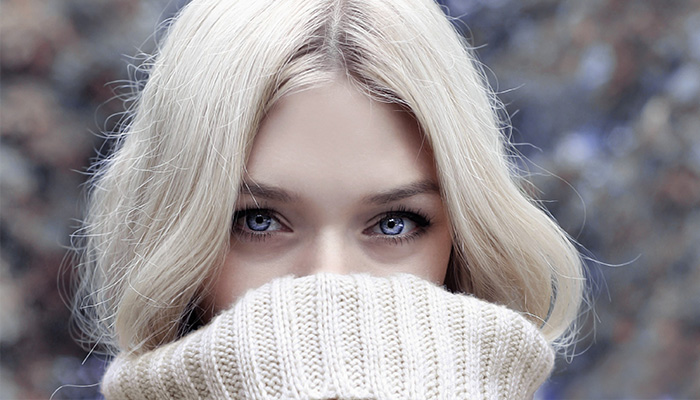 Close-up of a woman with blonde hair, styled with subtle makeup, covering her lower face with a beige sweater, focusing on her blue eyes. - K. Charles & Co. in San Antonio and Schertz, TX