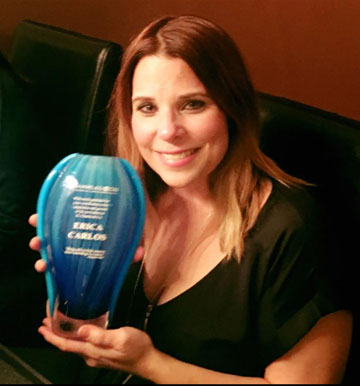 Woman smiling, holding a blue award with "premios juventud" and names "erika y carlos" inscribed on it. - K. Charles & Co. in San Antonio and Schertz, TX