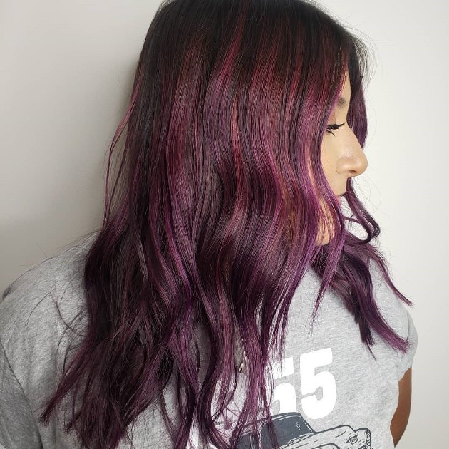 Side profile of a person with long, wavy hairstyle dyed in shades of purple and burgundy, wearing a grey t-shirt. - K. Charles & Co. in San Antonio and Schertz, TX