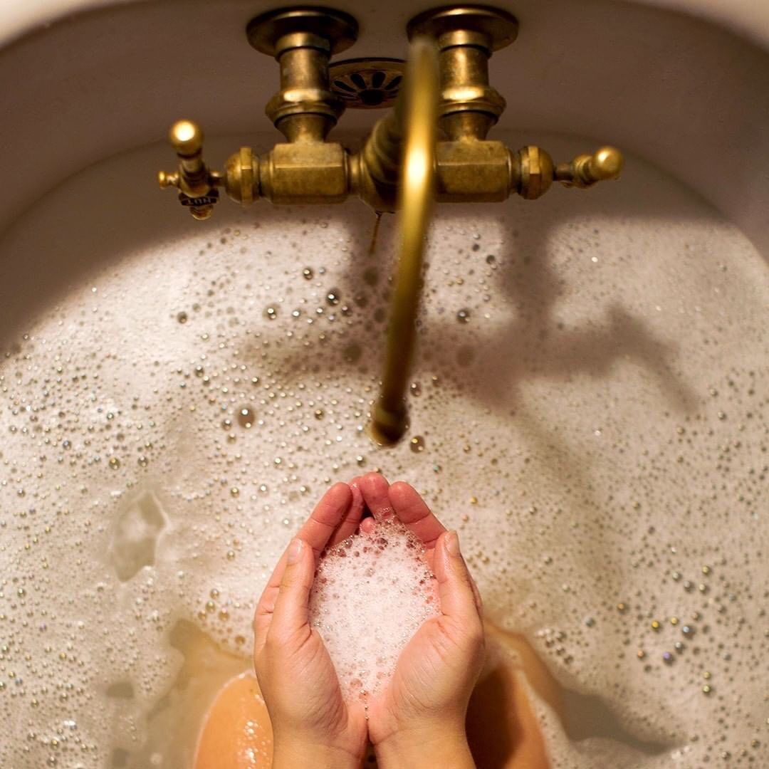 A person's cupped hands holding soapy water under a running antique brass faucet in a hair color-filled sink. - K. Charles & Co. in San Antonio and Schertz, TX