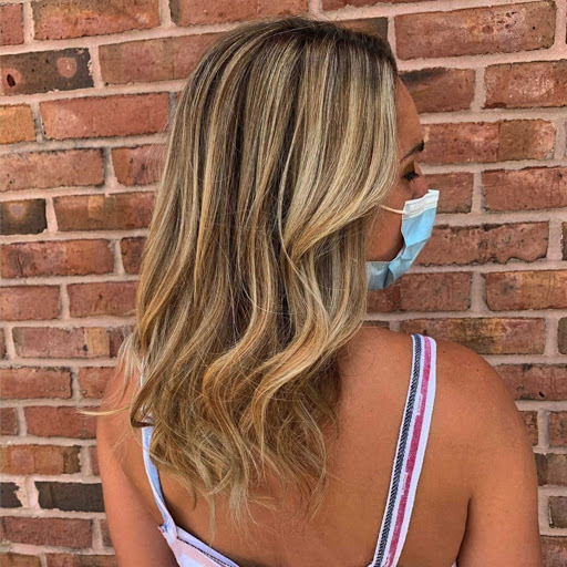 Woman wearing a mask lowered on her chin, showcasing her salon-finished hairstyle against a brick wall background. - K. Charles & Co. in San Antonio and Schertz, TX