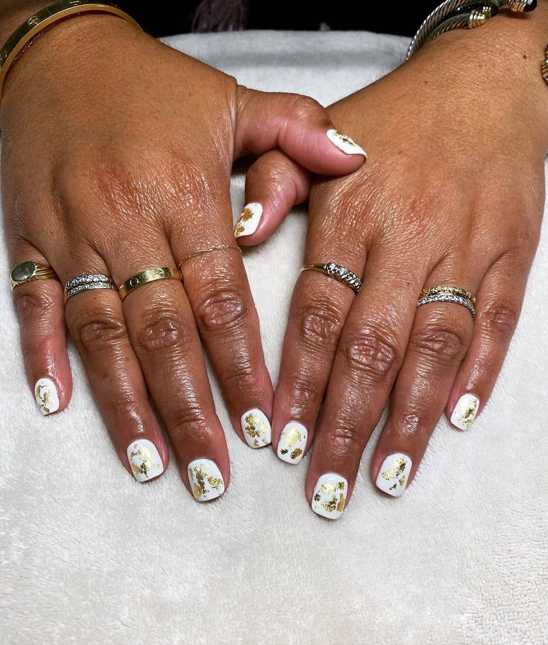 Two hands with long, manicured nails featuring white polish and floral designs, adorned with multiple rings on the fingers, resting on a white surface. - K. Charles & Co. in San Antonio and Schertz, TX