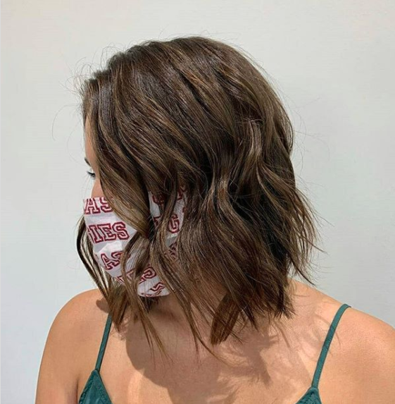 Woman with a medium-length wavy brown hairstyle wearing a mask with red text design, facing away from the camera against a plain background. - K. Charles & Co. in San Antonio and Schertz, TX