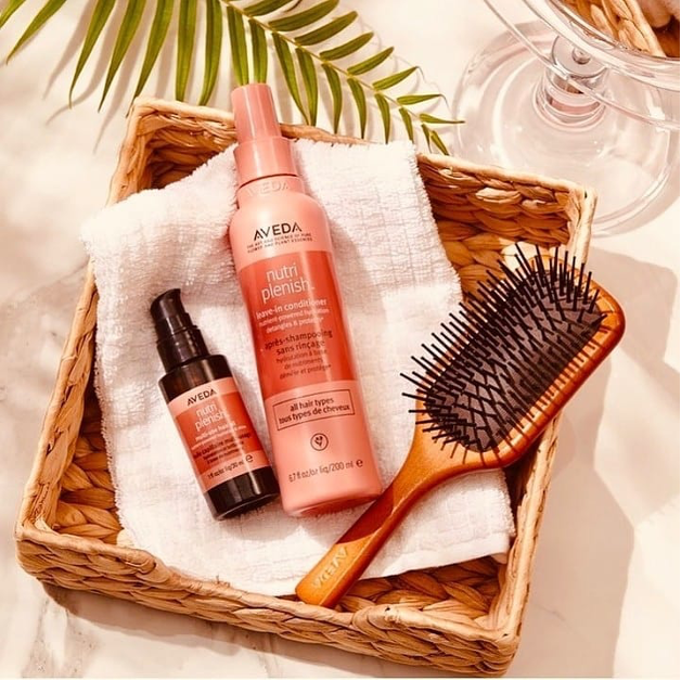 A wicker basket containing Aveda hair products, a towel, and a paddle brush, arranged neatly on a sunny surface at a salon. - K. Charles & Co. in San Antonio and Schertz, TX