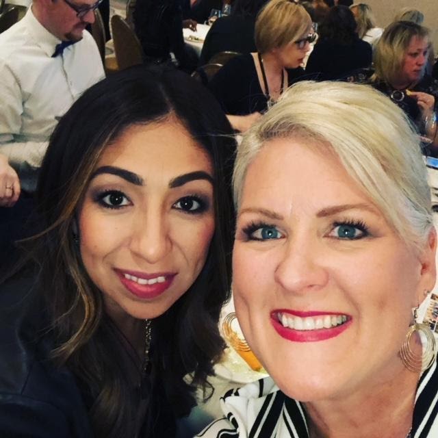 Two women smiling for a selfie at a crowded event, one with light hair and one with dark hair, both dressed in evening wear. - K. Charles & Co. in San Antonio and Schertz, TX