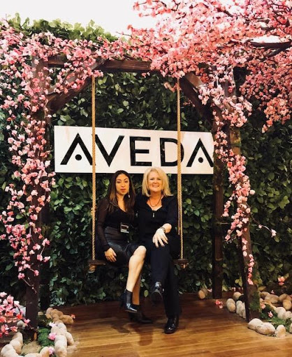 Two women sitting on a swing under a floral arch with the sign "aveda" at a promotional event. - K. Charles & Co. in San Antonio and Schertz, TX
