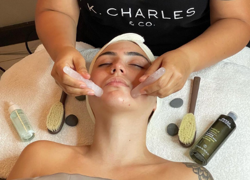 A person receiving a facial treatment with their eyes covered, as a therapist applies tools and products on their face in a salon setting. - K. Charles & Co. in San Antonio and Schertz, TX
