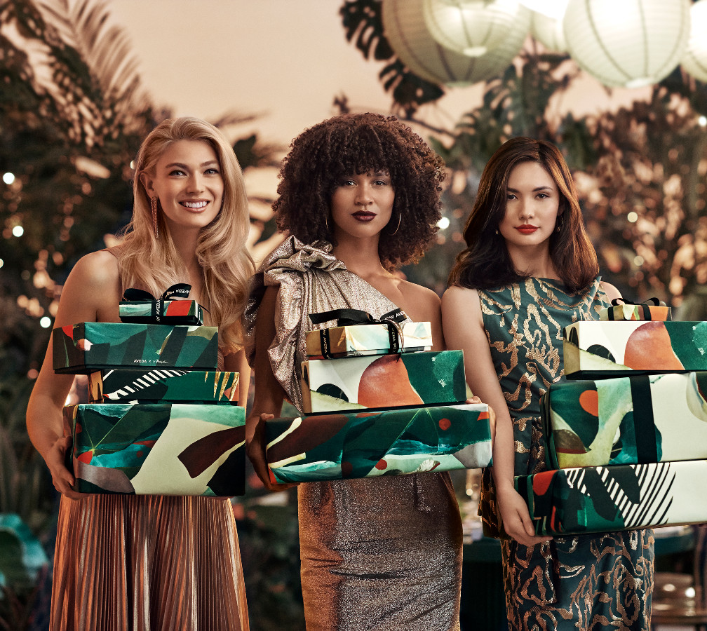 Three women holding gift boxes at a festive outdoor party, smiling and dressed in elegant evening wear. - K. Charles & Co. in San Antonio and Schertz, TX