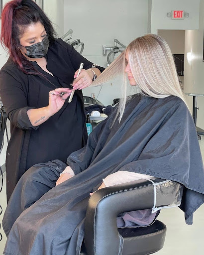 Hair stylist in a mask creating a new hairstyle for the blonde hair of a female client in a salon. - K. Charles & Co. in San Antonio and Schertz, TX