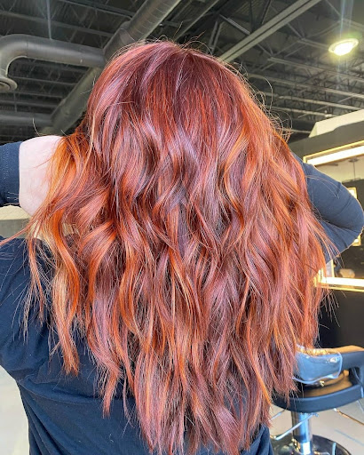 A woman with long, wavy auburn hair color, viewed from behind, in a salon setting. - K. Charles & Co. in San Antonio and Schertz, TX