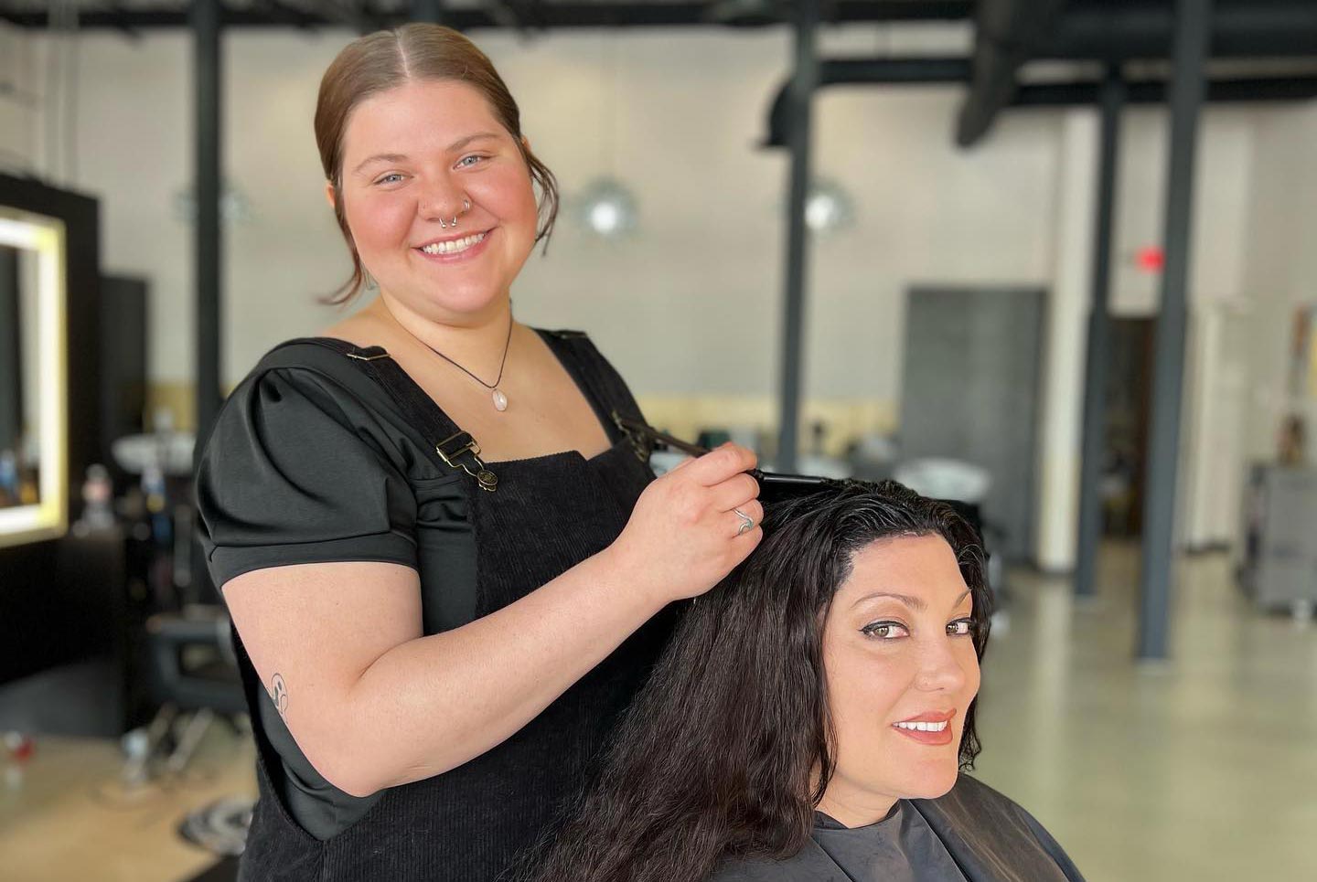 A hairstylist, smiling, works on a seated woman's hair color in a modern salon, both appearing happy. - K. Charles & Co. in San Antonio and Schertz, TX