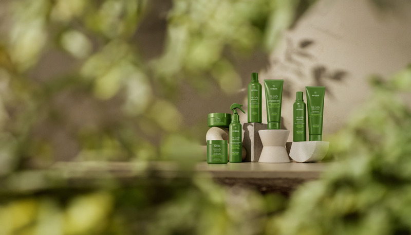 A collection of green skincare products arranged neatly on a reflective surface with a blurred green foliage background. - K. Charles & Co. in San Antonio and Schertz, TX