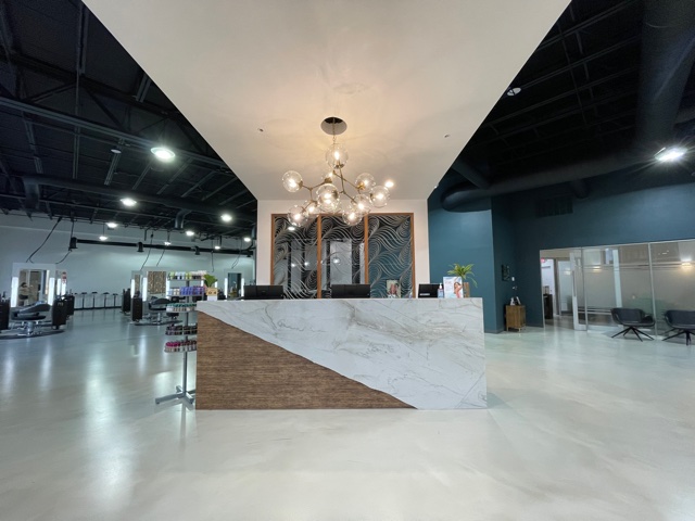 A modern salon reception area with a marble counter, contemporary chandelier, retail display on the left, and seating areas in the background. - K. Charles & Co. in San Antonio and Schertz, TX