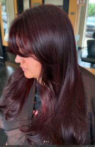 A person with long, straight, dark burgundy hair and layered bangs sitting in a salon chair. - K. Charles & Co. in San Antonio and Schertz, TX