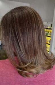 Person with shoulder-length, straight light brown hair with subtle blonde highlights, wearing a pink top, shown from the back in an indoor setting. - K. Charles & Co. in San Antonio and Schertz, TX