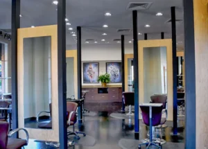 Modern hair salon interior with large mirrors, salon chairs, and black flooring. Artwork and a plant decorate the back wall. The space is well-lit with overhead lights. - K. Charles & Co. in San Antonio and Schertz, TX