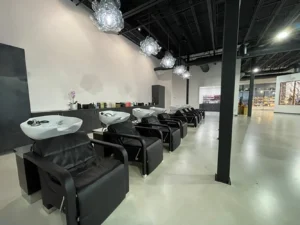 A row of black salon shampoo chairs with sinks in a modern, minimalist hair salon featuring pendant lights and a polished concrete floor. - K. Charles & Co. in San Antonio and Schertz, TX