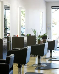 Three modern black salon chairs and styling stations with mirrors in a brightly lit hair salon, featuring minimal decor and large windows. - K. Charles & Co. in San Antonio and Schertz, TX