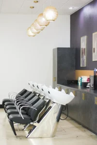 A row of black salon chairs with white washbasins, pendant lights above, and shelves with hair products and equipment along the wall. - K. Charles & Co. in San Antonio and Schertz, TX