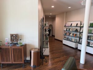 A modern salon interior with shelves of beauty products, a coat rack, a wooden cabinet, and a trash bin on hardwood floors under bright lighting. - K. Charles & Co. in San Antonio, TX