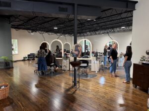 People are getting haircuts and talking in a modern salon with wooden floors, mirrors, and styling stations. - K. Charles & Co. in San Antonio, TX