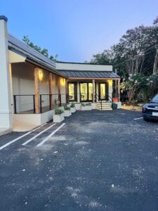 Single-story building with a covered porch, potted plants, and exterior lights, next to a parking lot with one parked car at dusk. - K. Charles & Co. in San Antonio, TX