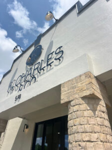 Exterior view of a light-colored building with stone columns, displaying a sign that reads “CHARLES” and “518” under bright daylight with a partly cloudy sky. - K. Charles & Co. in San Antonio, TX